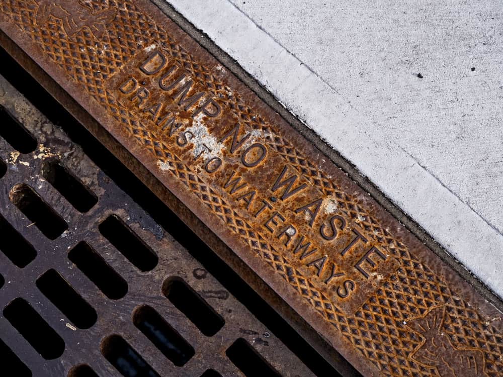 A rusted street drainage grate set in kerbside asphalt.